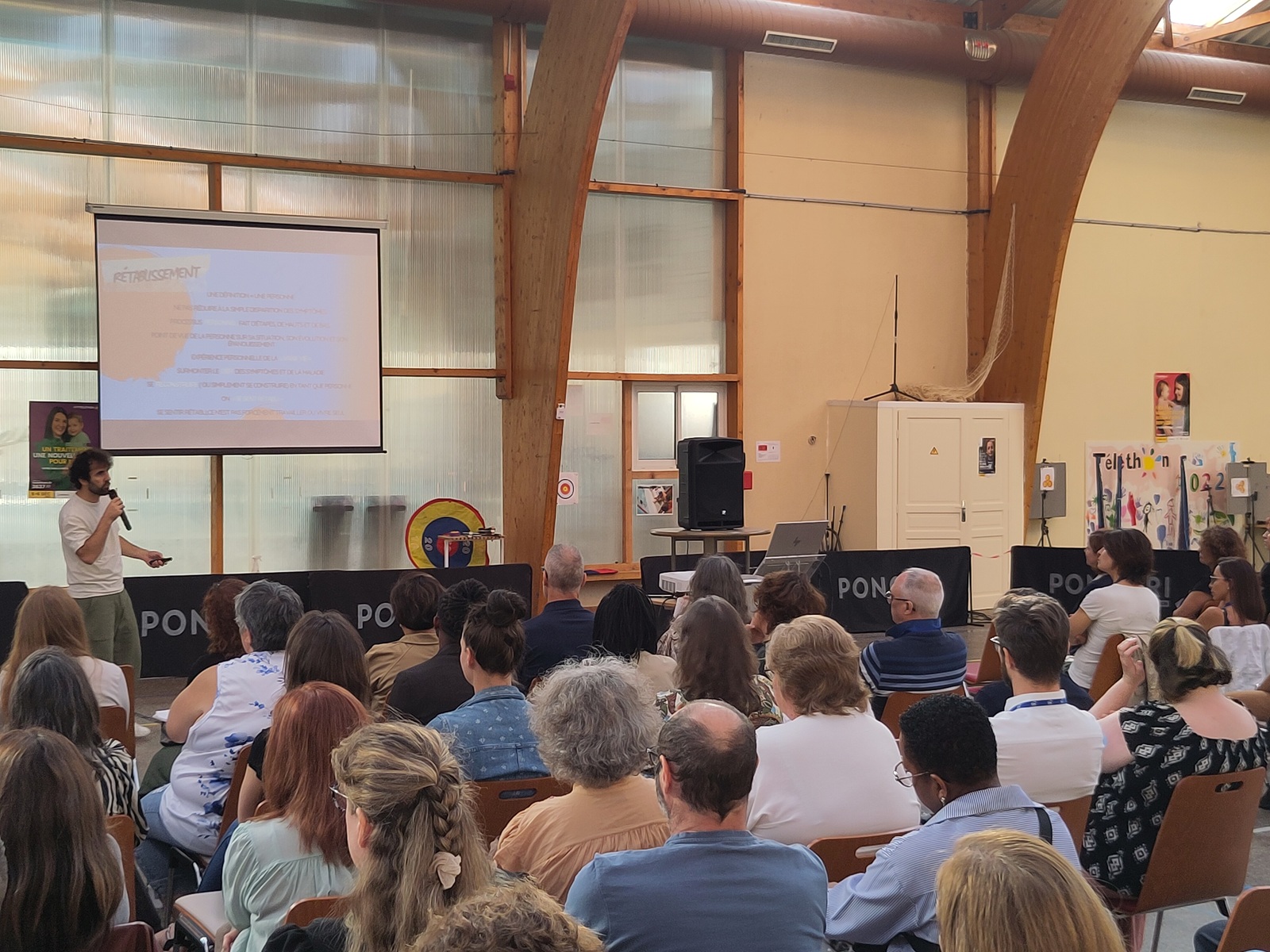 Une présentation se déroule devant un public nombreux et attentif, réuni dans une salle conviviale autour d’un intervenant et d’un écran de projection.
