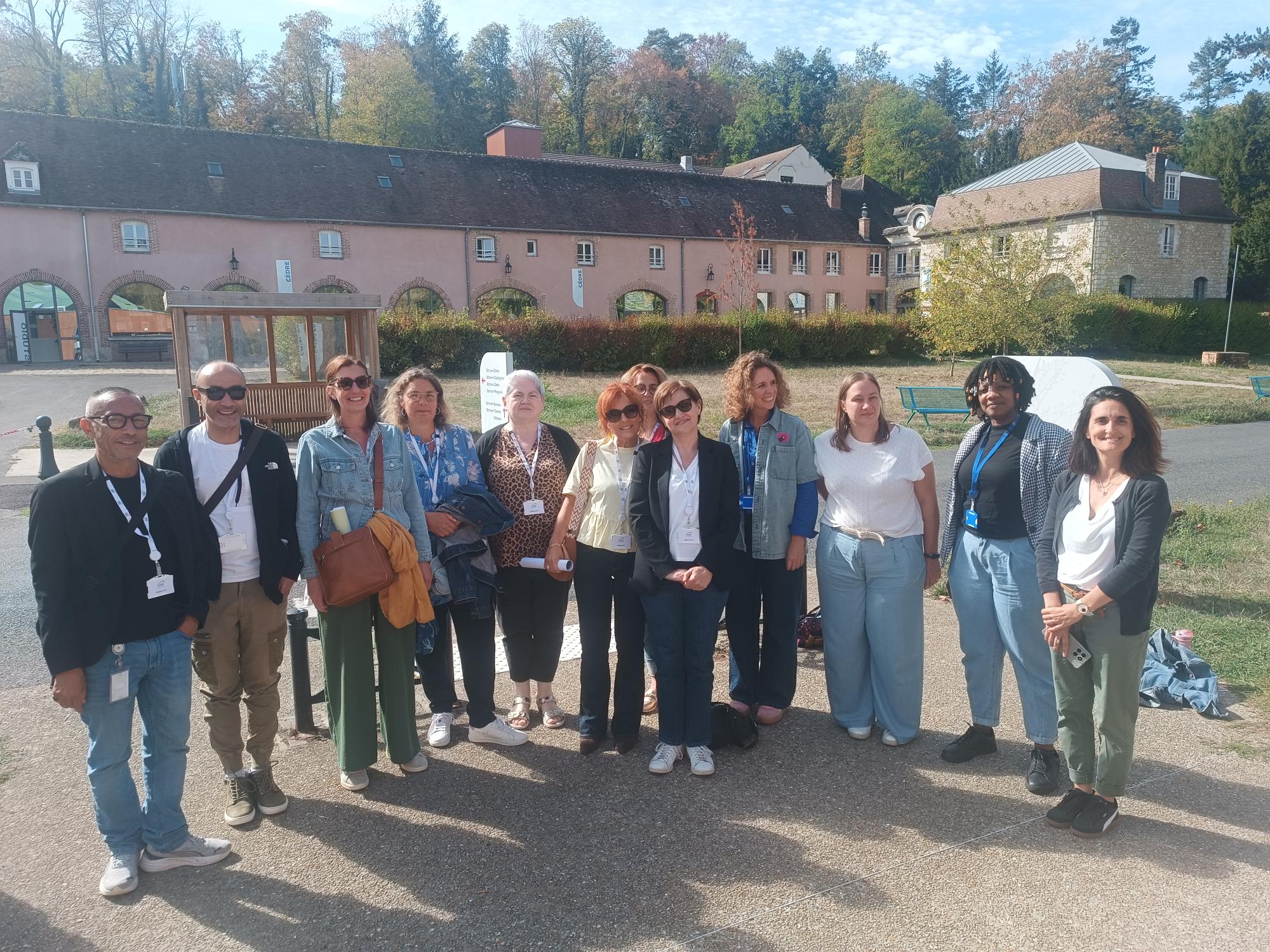 une douzaine de personnes rassemblées regardant l'objectif, en extérieur avec un bâtiment en arrière plan