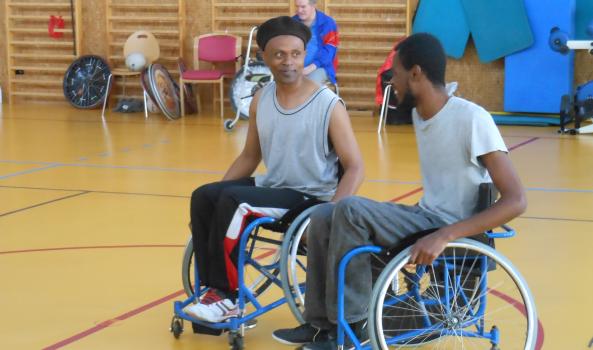 2 personnes en fauteuil roulant discutent au milieu d'un gymnase